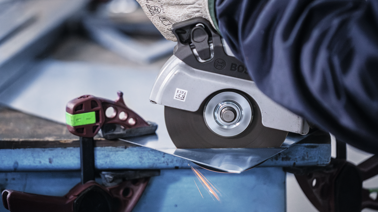 Đá cắt liên kết PRO Stainless Steel and Metal, 125 x 1 x 22,23 mm, thẳng Người mặc đồ bảo hộ đang cắt tấm kim loại bằng máy mài góc.