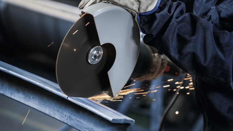 Đá cắt PRO Stainless Steel, 180 x 2 x 22,23 mm Một người mặc đồ bảo hộ đang cắt kim loại bằng máy mài góc, tia lửa bắn ra.
