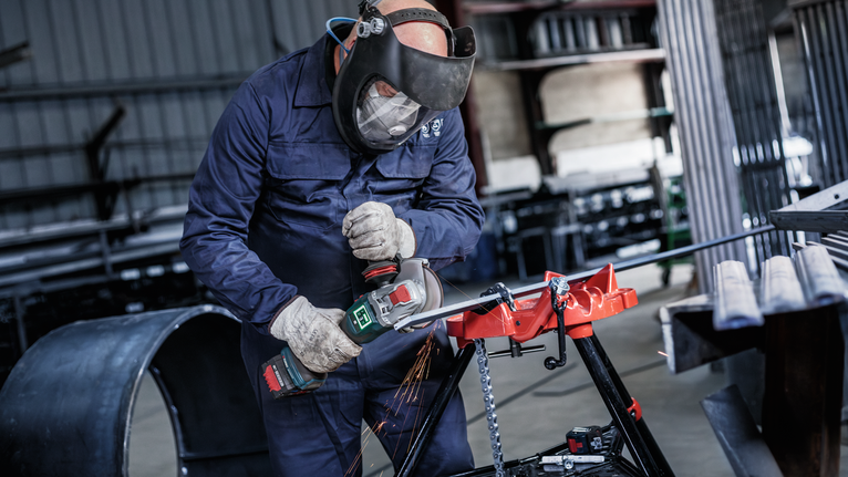 Đá cắt liên kết PRO Metal, 125 x 1,6 x 22,23 mm, X-Lock Một người mặc đồ bảo hộ sử dụng máy mài góc để cắt kim loại, tạo ra tia lửa điện.