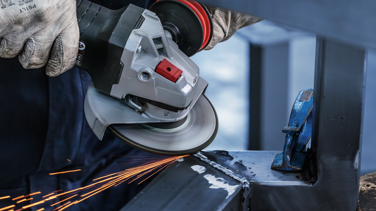 Đĩa mài PRO Stainless Steel, 125 x 6 x 22,23 mm Một người mặc đồ bảo hộ sẽ mài kim loại, tạo ra tia lửa.