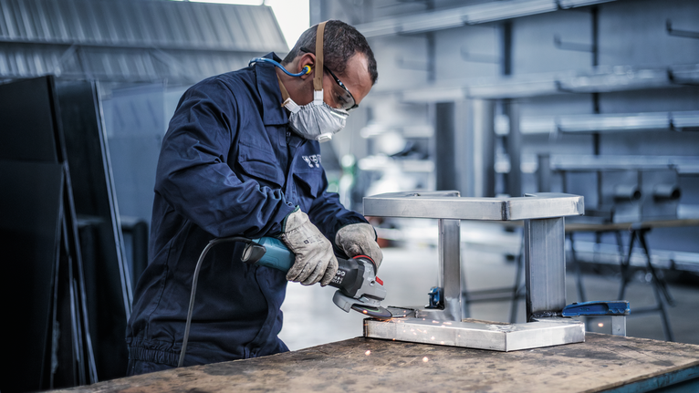 Đĩa mài PRO Stainless Steel, 125 x 6 x 22,23 mm Người mặc đồ bảo hộ mài khung kim loại, tạo ra tia lửa.