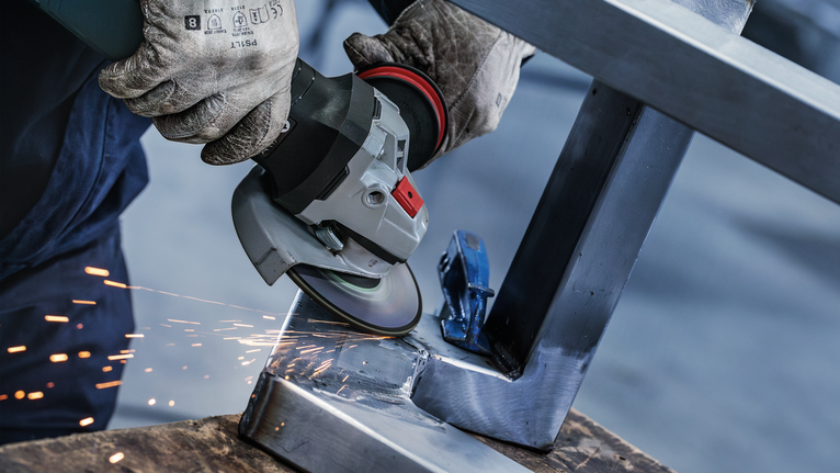 Đĩa mài PRO Stainless Steel, 125 x 6 x 22,23 mm Một người mặc đồ bảo hộ mài khung kim loại, tạo ra tia lửa bắn ra.