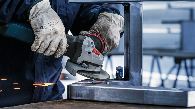 Đĩa mài PRO Stainless Steel, 125 x 6 x 22,23 mm Một người mặc đồ bảo hộ đang mài một thanh kim loại bằng máy mài góc.