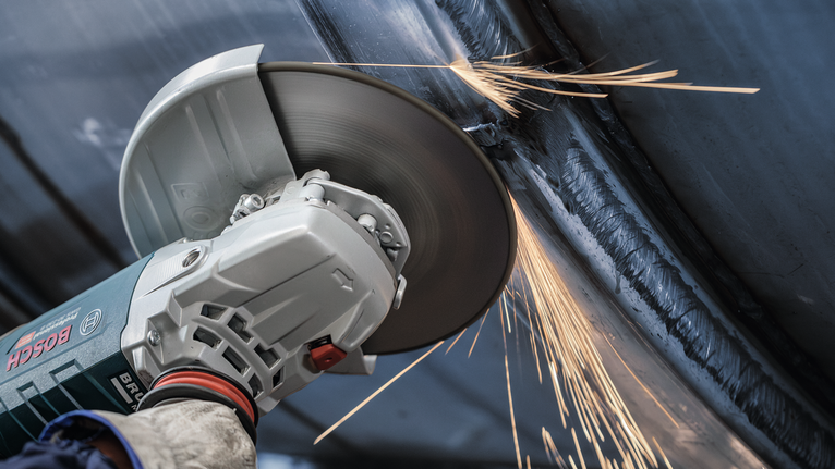 Đĩa mài PRO Stainless Steel, 180 x 6 x 22,23 mm Một người mặc đồ bảo hộ sẽ mài kim loại, tạo ra tia lửa.