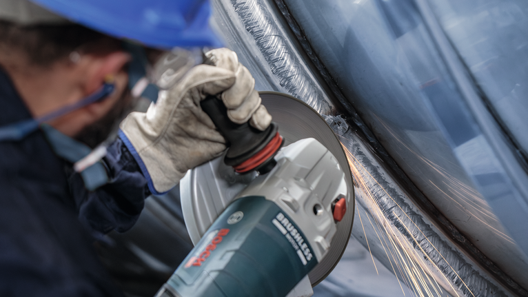 Đĩa mài PRO Stainless Steel, 180 x 6 x 22,23 mm Một người mặc đồ bảo hộ sẽ mài kim loại, tạo ra tia lửa.