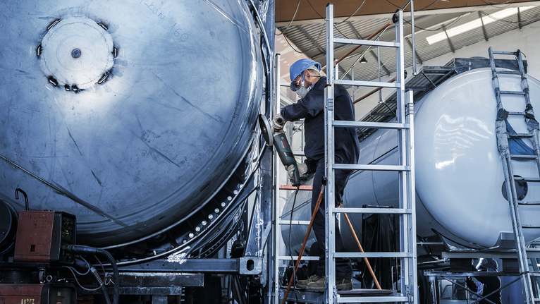 Đĩa mài PRO Stainless Steel, 180 x 6 x 22,23 mm Một người mặc đồ bảo hộ đang sử dụng dụng cụ điện trên một thùng kim loại lớn.