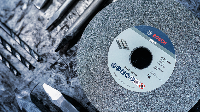 Bánh mài lớn được đặt giữa một số mũi khoan kim loại trên bề mặt làm việc thô ráp.