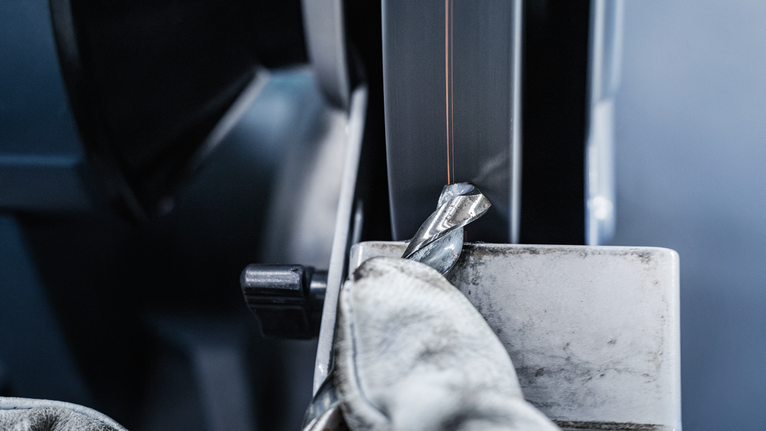 Người đeo thiết bị an toàn đang mài mũi khoan trên máy mài.