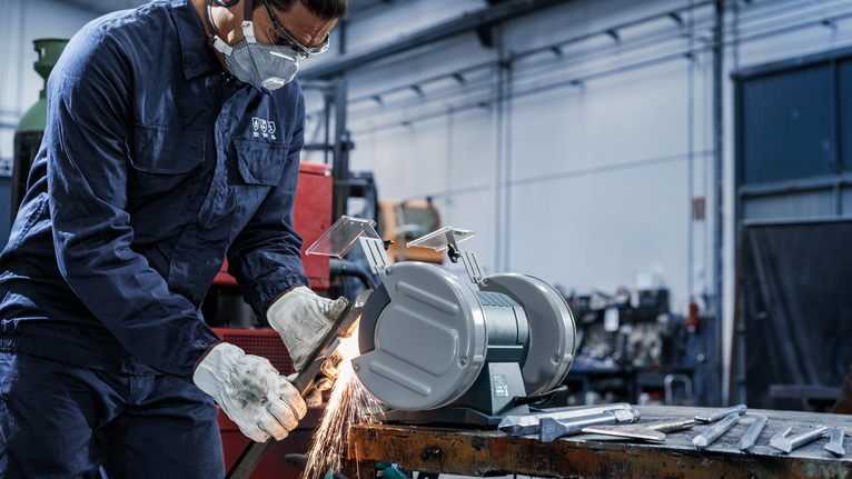 Người mặc đồ bảo hộ đang mài kim loại trên máy mài trong xưởng.