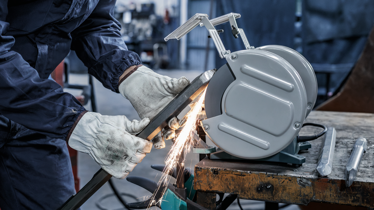 Một người mặc đồ bảo hộ đang mài kim loại, tạo ra tia lửa trên bàn làm việc.