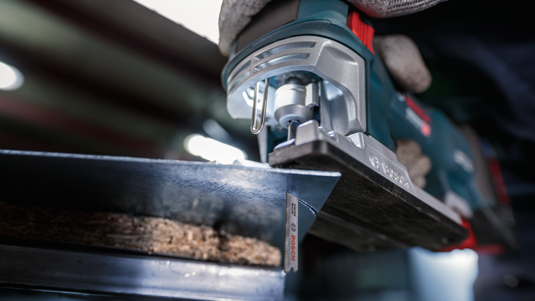 Người mặc đồ bảo hộ đang cắt gỗ bằng máy cưa lọng.