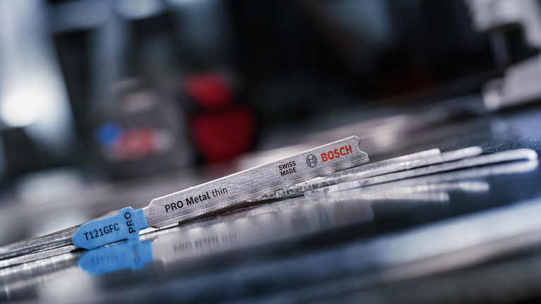 Lưỡi cưa lọng bằng kim loại nằm trên bề mặt kim loại phản chiếu trong một xưởng.