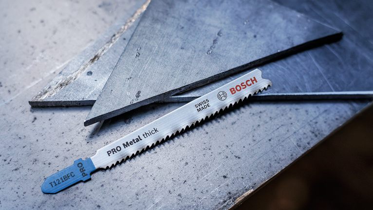 Lưỡi cưa kim loại nằm trên bề mặt thép bên cạnh các tấm kim loại đã cắt.