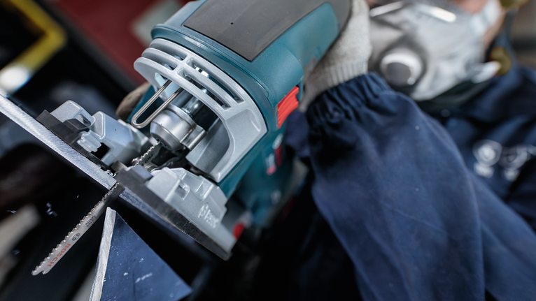 Người mặc đồ bảo hộ đang sử dụng máy cưa lọng để cắt kim loại.