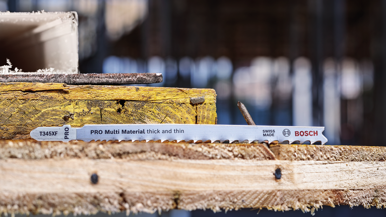 Lưỡi cưa lọng PRO Multi Material thick and thin T345XF, 132 mm, 5 chiếc Lưỡi cưa lọng nằm trên những tấm ván gỗ xếp chồng lên nhau tại một công trường xây dựng.