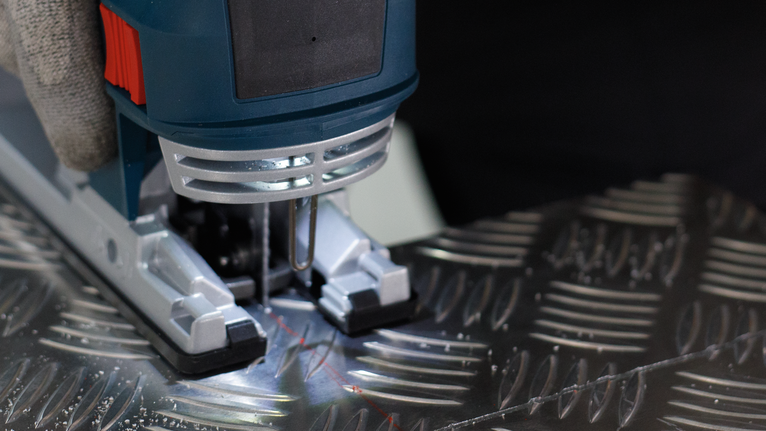 Lưỡi cưa lọng PRO Alu T127D, 100 mm, 5 chiếc Người mặc đồ bảo hộ đang vận hành máy cưa lọng để cắt tấm kim loại có hoa văn.