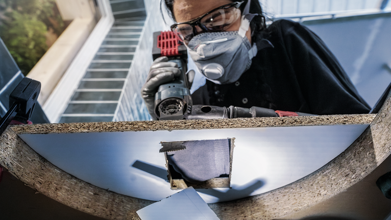 Người đeo thiết bị an toàn khoan lỗ trên tấm ván gỗ.