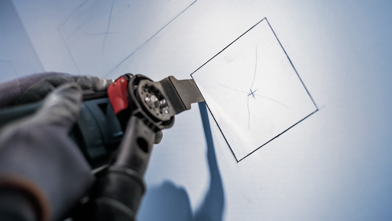 Người đeo thiết bị an toàn sử dụng dụng cụ điện để cắt hình vuông trên vách thạch cao.