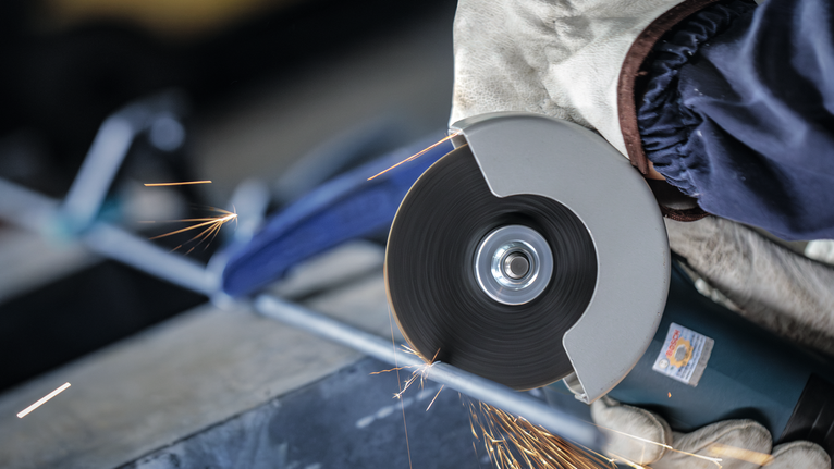 Người đeo thiết bị an toàn mài một thanh kim loại bằng dụng cụ cắt.