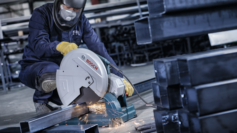 Một công nhân mặc đồ bảo hộ đang cắt ống kim loại bằng máy cưa điện, tạo ra tia lửa.