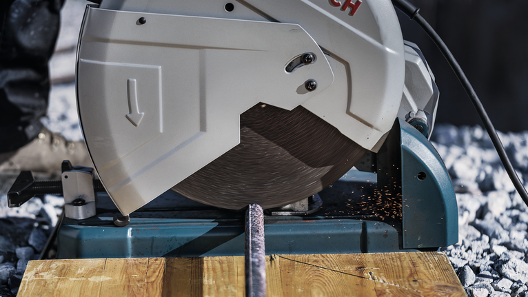 Lưỡi cưa kim loại cắt xuyên qua thanh thép, tạo ra tia lửa trên bề mặt gỗ.