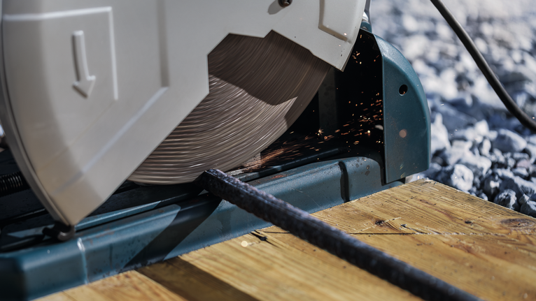 Lưỡi cưa cắt một thanh kim loại trên một bệ gỗ.