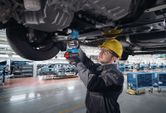 Một người mặc thiết bị an toàn đang sử dụng cờ lê lực không dây để tháo khung xe ô tô.