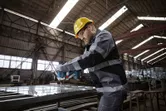 Một người mặc thiết bị an toàn sử dụng dụng cụ điện để vặn chặt bu lông trên khung kim loại.