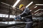 Một người mặc thiết bị an toàn sử dụng dụng cụ điện để vặn chặt bu lông trên khung kim loại.