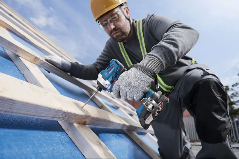 Một người mặc đồ bảo hộ sử dụng máy khoan không dây để vặn vít vào thanh gỗ.