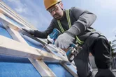 Một người mặc thiết bị an toàn sử dụng máy khoan không dây để đóng chặt gỗ trên bề mặt nghiêng.