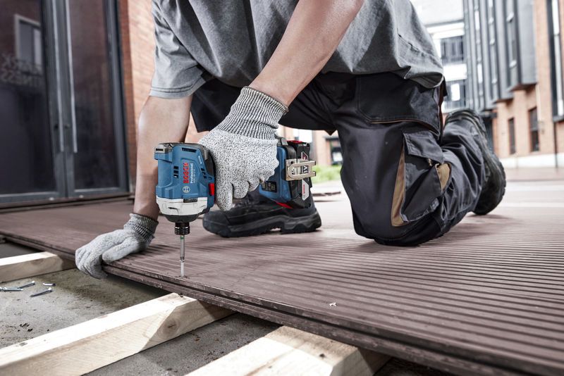 Một người mặc đồ bảo hộ sử dụng máy khoan không dây để cố định ván sàn.