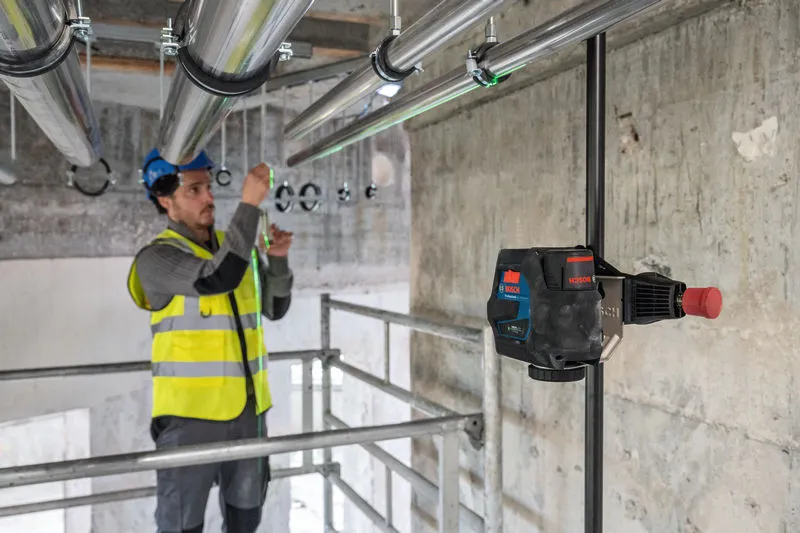 Một người mặc thiết bị an toàn đang căn chỉnh các đường ống bằng dụng cụ cân bằng laser.