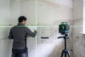 Một người đang căn chỉnh các viên gạch trên tường bằng công cụ cân bằng laser màu xanh lá cây trên giá ba chân.