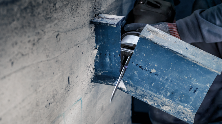 Người mặc đồ bảo hộ đang cắt một thanh thép bằng dụng cụ điện.