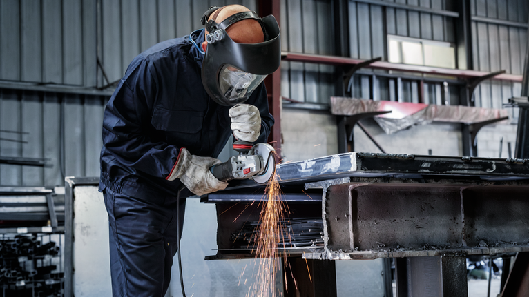 Đĩa mài PRO Metal, 150 x 6 x 22,23 mm Một người mặc đồ bảo hộ sẽ mài kim loại, tạo ra tia lửa bắn ra.