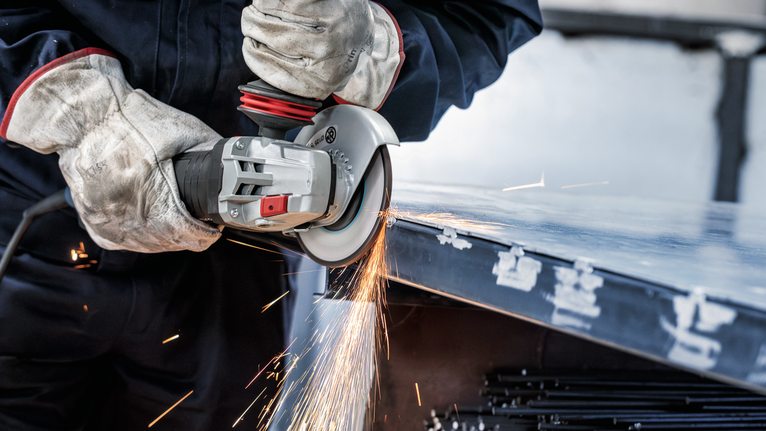Đĩa mài PRO Metal, 150 x 6 x 22,23 mm Một người đeo thiết bị an toàn đang mài cạnh của một tấm kim loại bằng một dụng cụ điện.