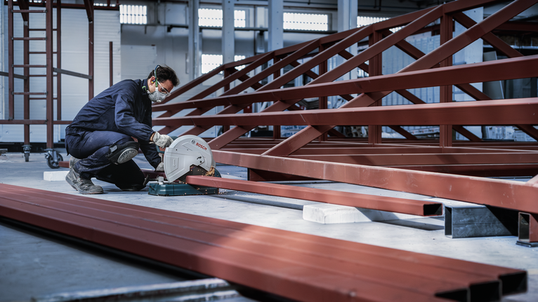 Đá cắt PRO Metal, 305 x 3 x 25,4 mm Một người mặc đồ bảo hộ đang cắt một thanh thép bằng máy cưa tròn trong một nhà máy.