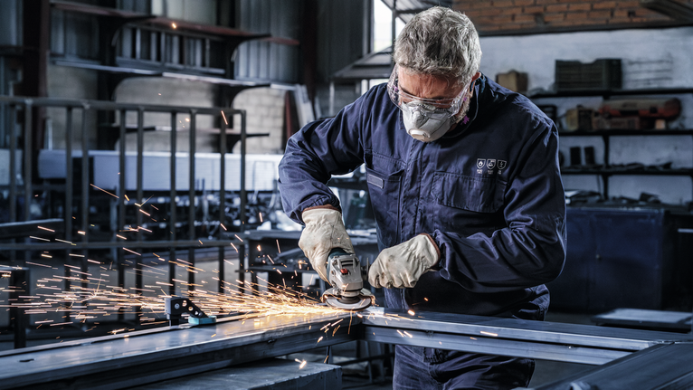 Người mặc đồ bảo hộ lao động mài kim loại, tạo ra tia lửa trong xưởng.