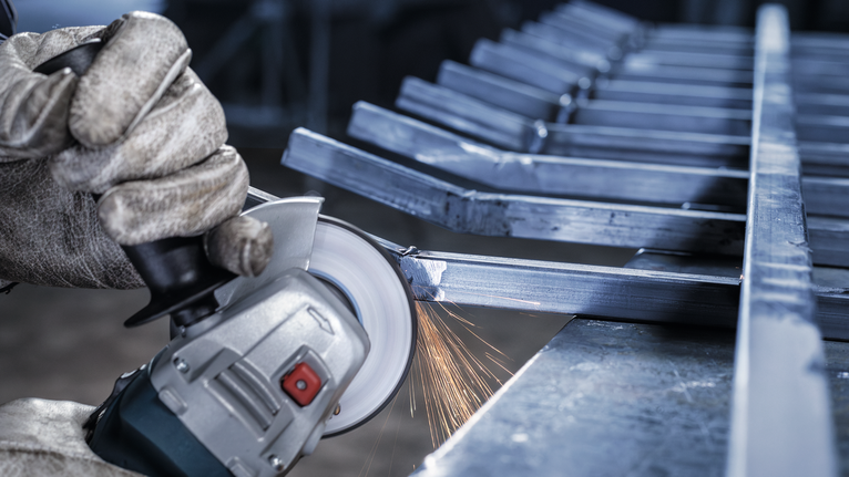 Người đeo thiết bị an toàn mài các thanh kim loại bằng máy mài góc, tạo ra tia lửa.