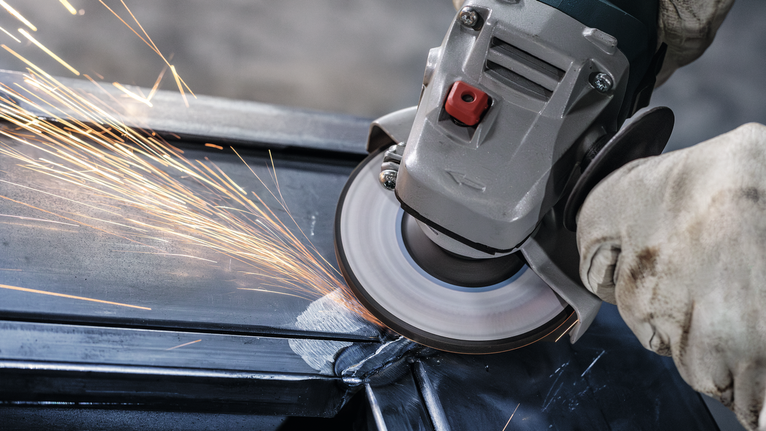 Người đeo thiết bị an toàn mài một thanh kim loại bằng máy mài góc.