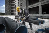 Một người đeo thiết bị an toàn đang sử dụng máy mài góc không dây để cắt một ống nhựa lớn.