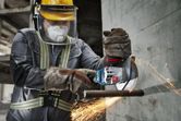 Một người mặc đồ bảo hộ đang cắt thép vào tường bằng máy mài góc không dây.