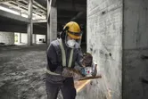 Một người mặc thiết bị an toàn đang sử dụng máy mài góc không dây để cắt cốt thép trên tường bê tông.