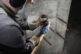 Một người mặc thiết bị an toàn đang mài thanh thép lộ ra trên tường bê tông.