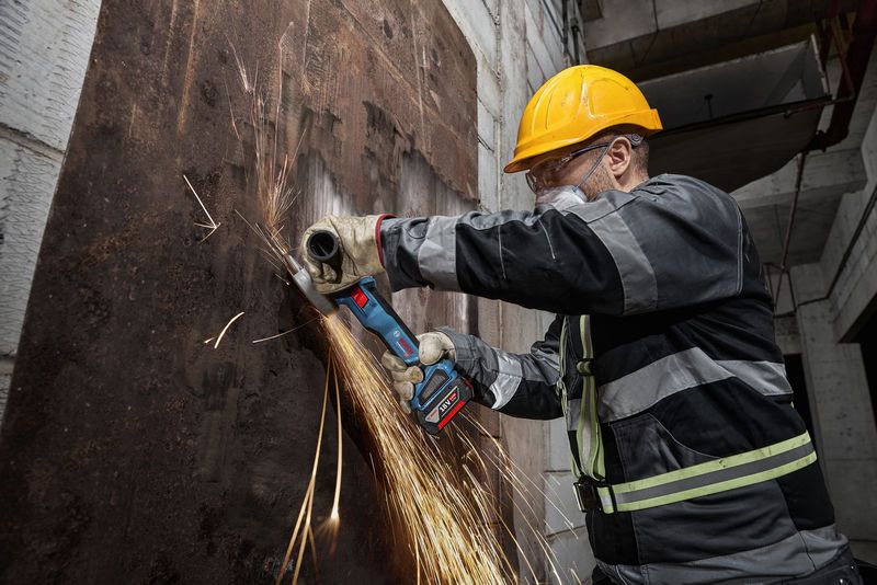 Một người mặc đồ bảo hộ đang mài một tấm kim loại bị gỉ bằng máy mài góc không dây.