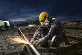 Một người mặc đồ bảo hộ đang sử dụng máy mài góc để cắt đường ray xe lửa.