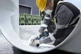 Một người mặc đồ bảo hộ đang mài phần bên trong của một ống kim loại lớn.