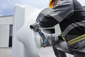 Một người đeo thiết bị an toàn đang mài một ống kim loại lớn bằng máy mài góc không dây.
