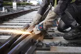 Một người mặc đồ bảo hộ đang mài đường ray xe lửa bằng máy mài góc không dây.